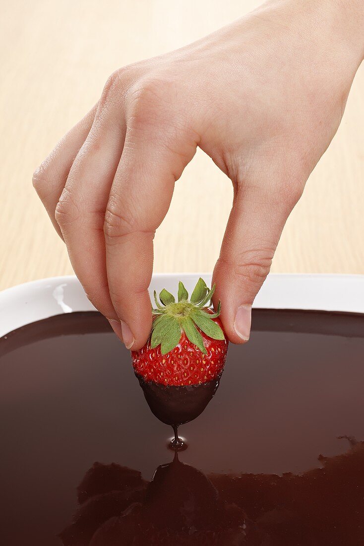 Hand dippt Erdbeere in Schokoladensauce