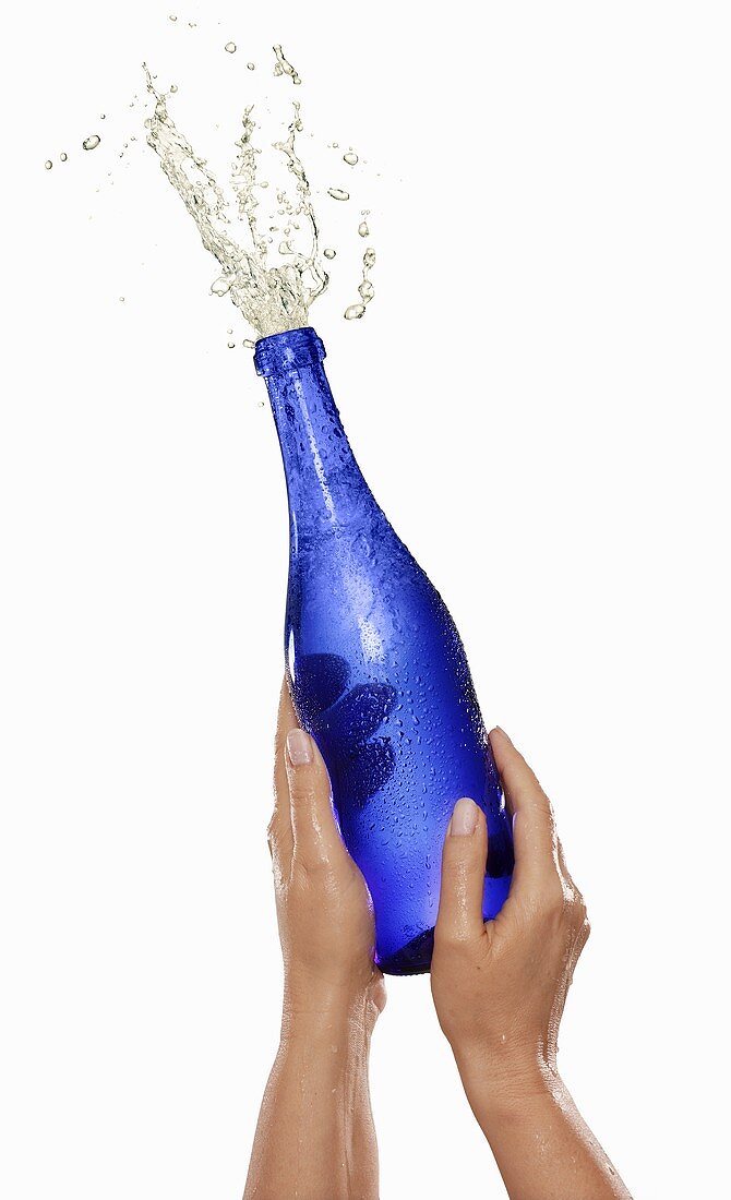 Hands holding a spraying champagne bottle
