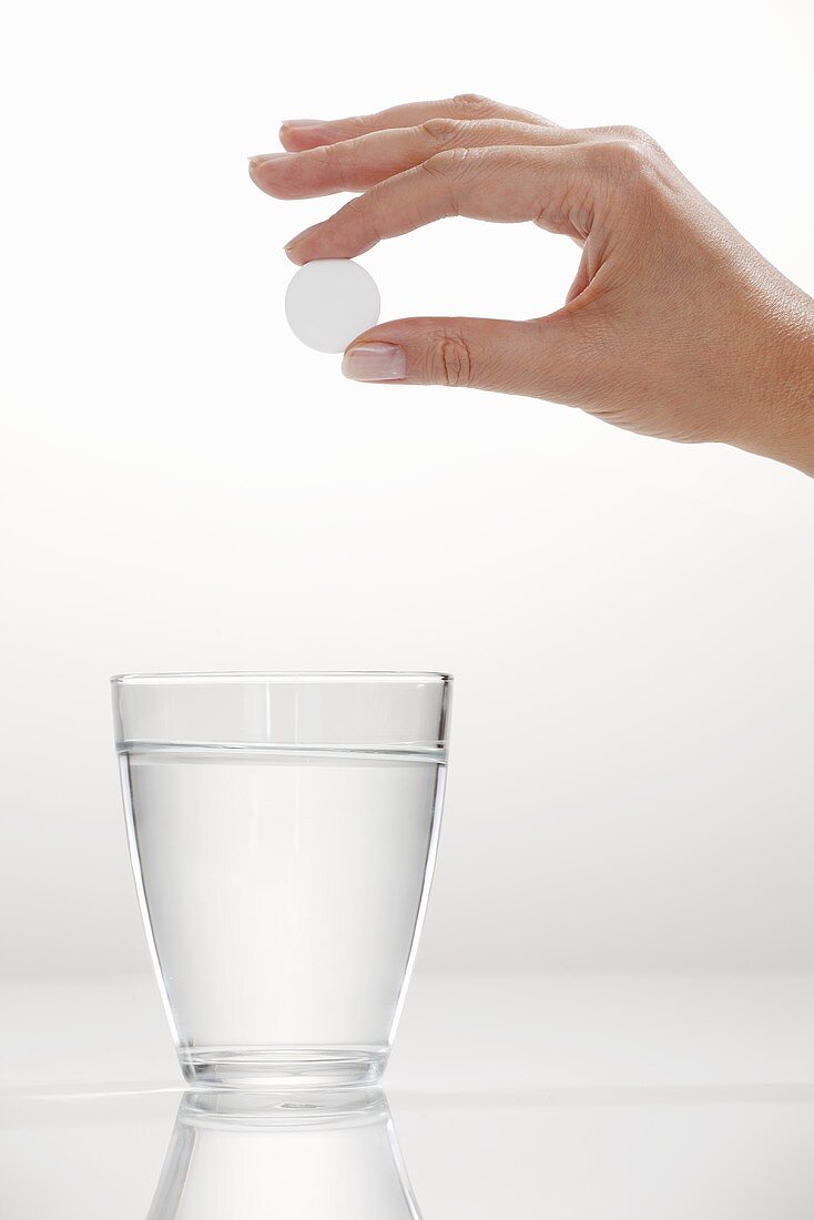 Hand hält Brausetablette über Wasserglas