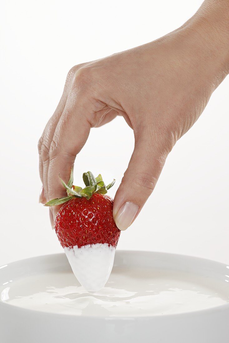 Hand dippt Erdbeere in Naturjoghurt