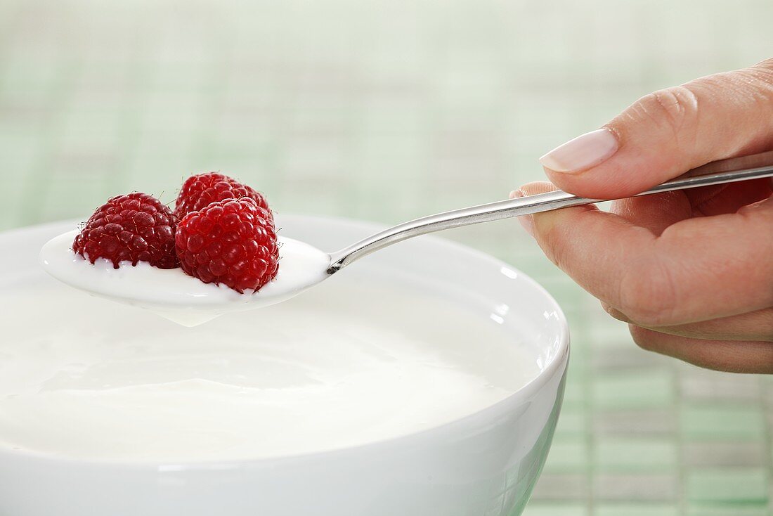 Hand holding a spoon of yogurt with raspberries