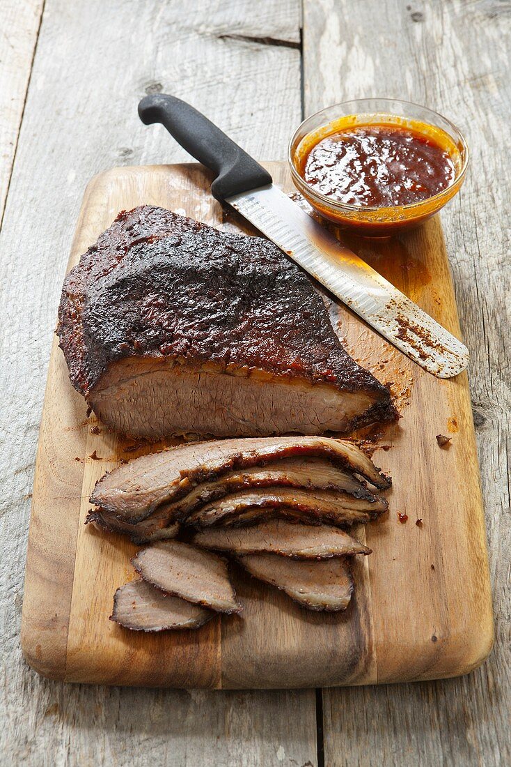 Partially Sliced Barbecue Brisket on a Cutting Board; Knife and Barbecue Sauce