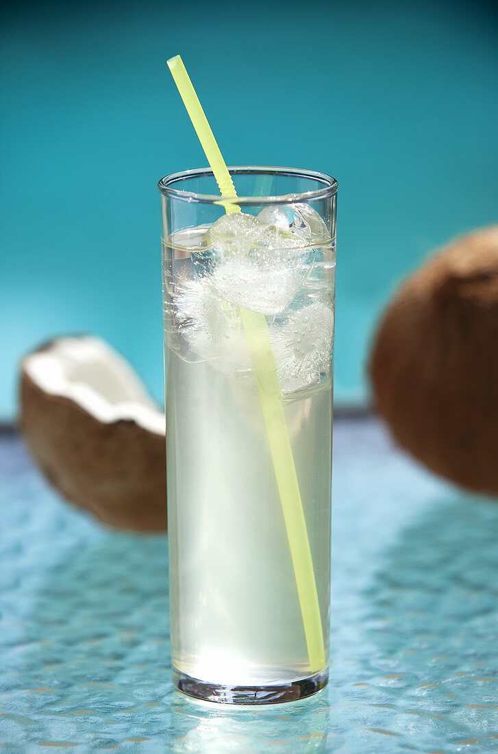 Ein Glas Kokoswasser mit Eiswürfeln und Strohhalm