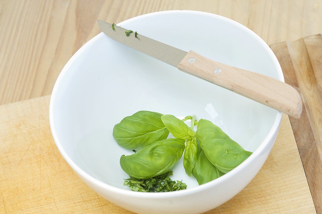 Partially chopped basil in a bowl with a knife