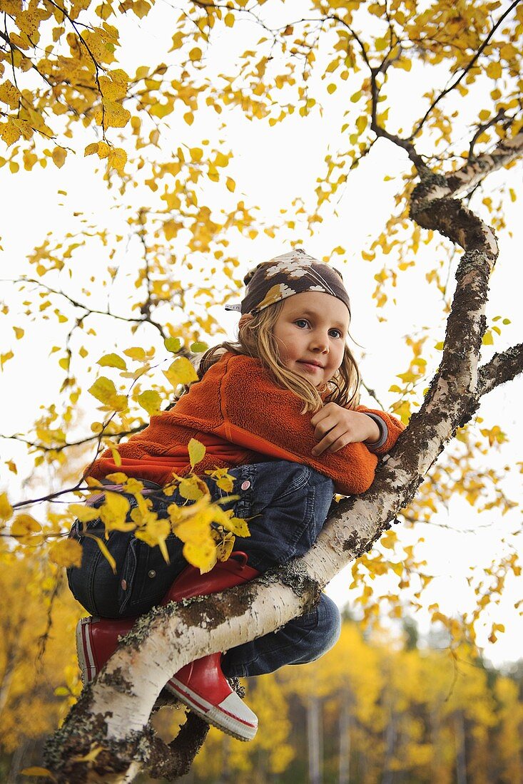 Mädchen sitzt am herbstlichen Baum