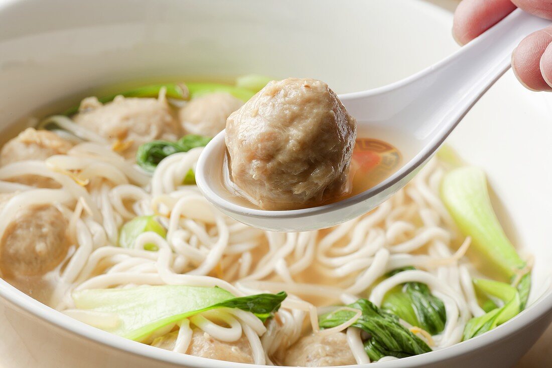 Shanghai-Nudelsuppe mit Pak Choi und Hackbällchen (Hand hält Löffel mit Hackbällchen)