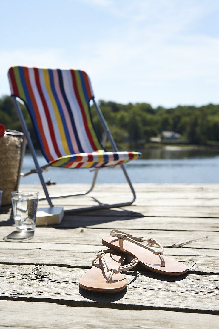 Deck chair and flip flops on a wooden jetty on the lake