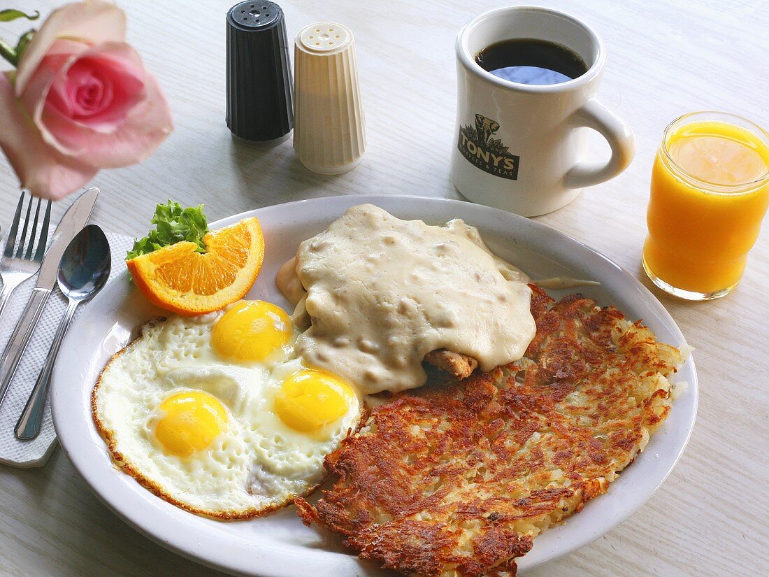 Grosses Frühstück mit Spiegeleiern, Hähnchenschnitzel mit Gravy, Rösti, Kaffee und Saft (USA)