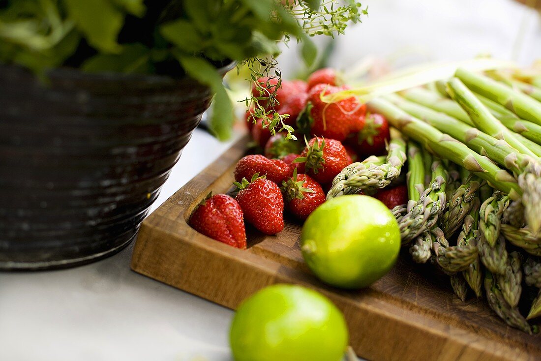 Erdbeeren, grüner Spargel und Limetten auf Holzbrett
