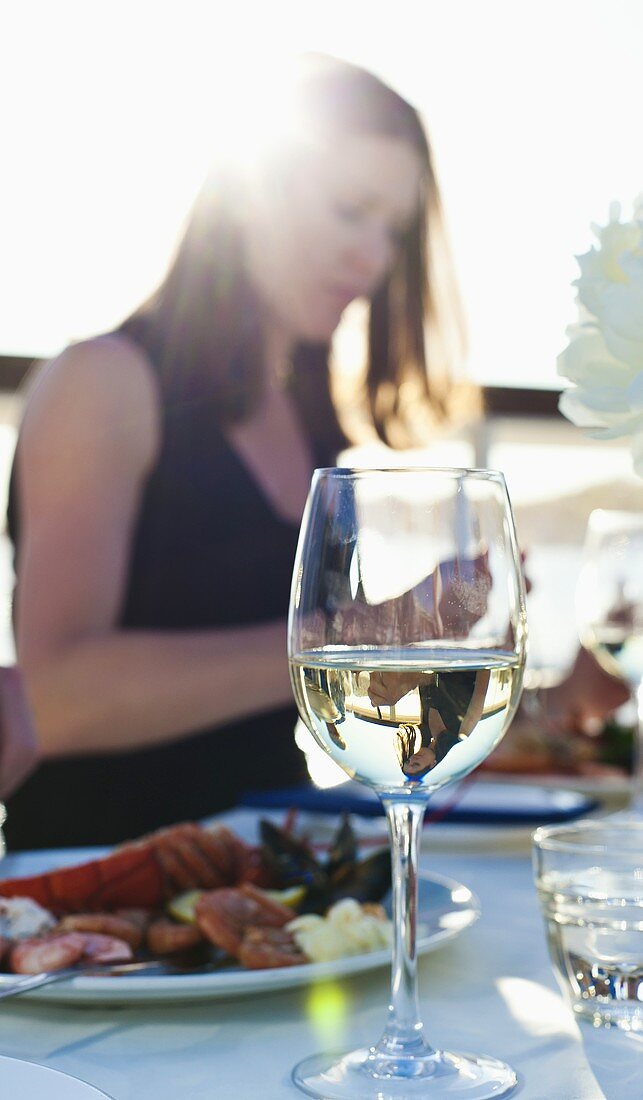Weissweinglas, im Hintergrund Frau beim Essen