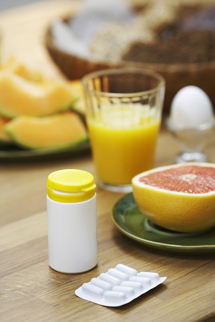 Breakfast with orange juice, fruit and egg with tablets in the foreground