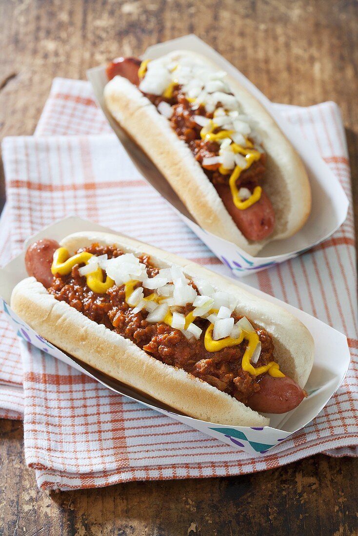 Zwei Chili Dogs mit Zwiebeln und Senf in Pappschälchen