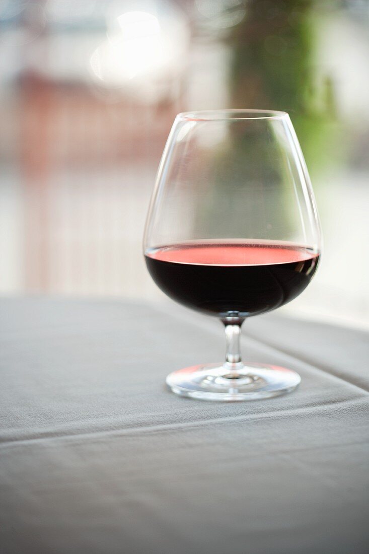 Glas Rotwein auf Tisch mit weisser Tischdecke