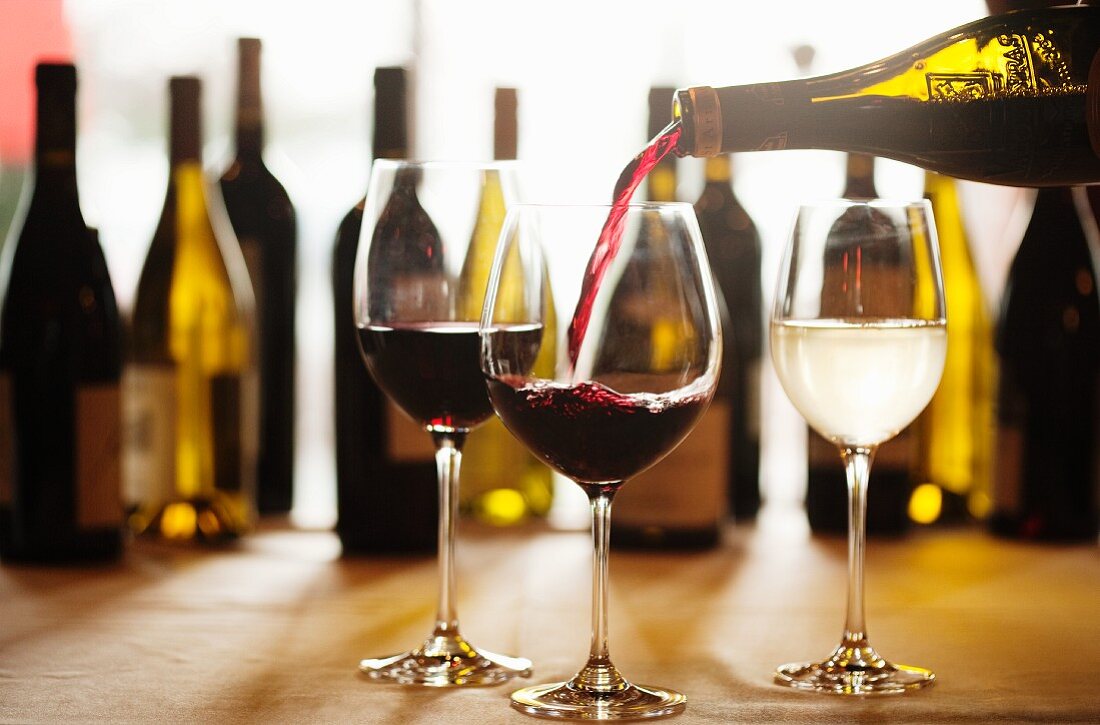 Rotwein in Glas einschenken, verschiedene Weingläser und Weinflaschen