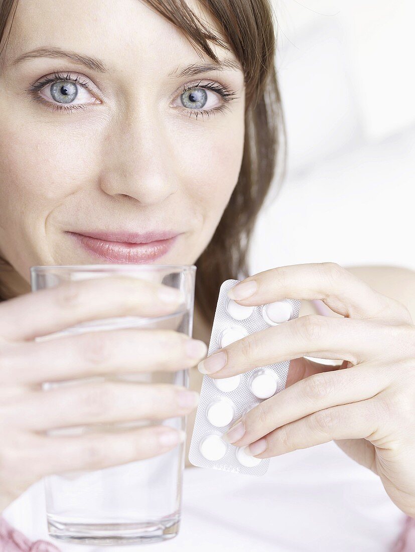 Frau hält Wasserglas und Tabletten