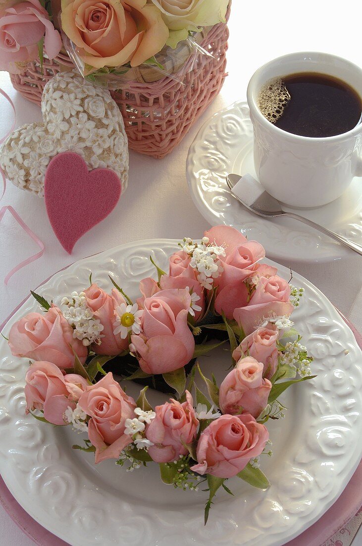 Heart-shaped wreath of roses on plate, cup of coffee