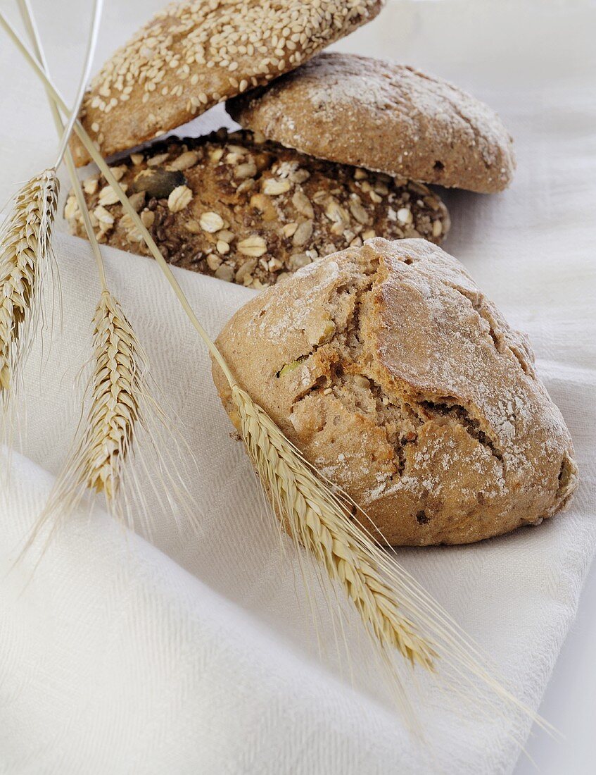 Assorted wholemeal rolls with cereal ears on linen cloth