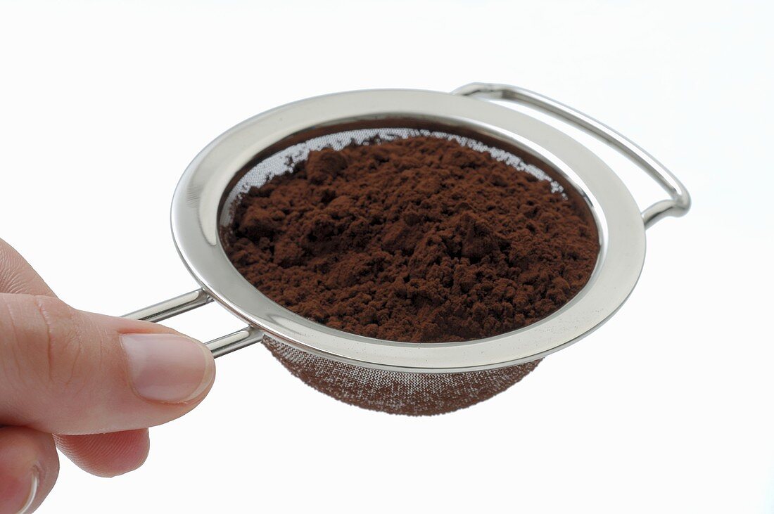 Hand holding a sieve full of cocoa powder