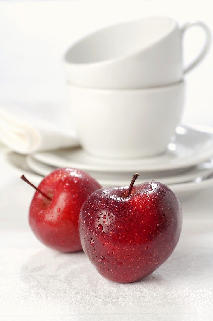 Zwei rote Äpfel mit Wassertropfen, Tassen im Hintergrund