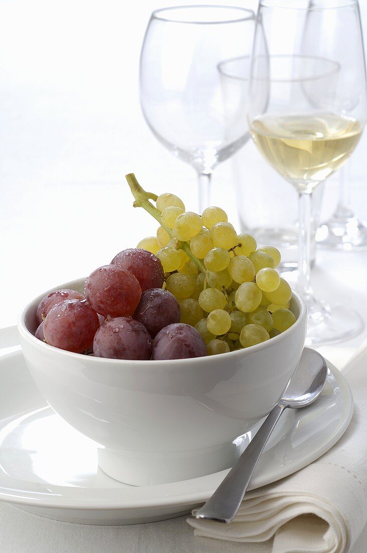 Fresh grapes in bowl, wine glasses in background