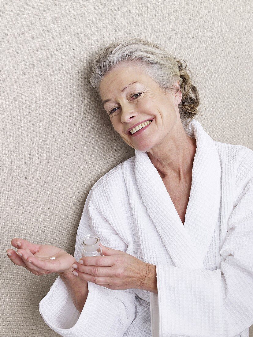 Ältere Frau im Bademantel mit Tabletten