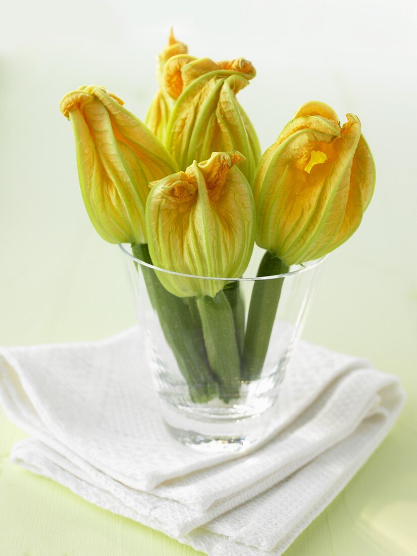 Five courgettes with flowers in a glass on a napkin