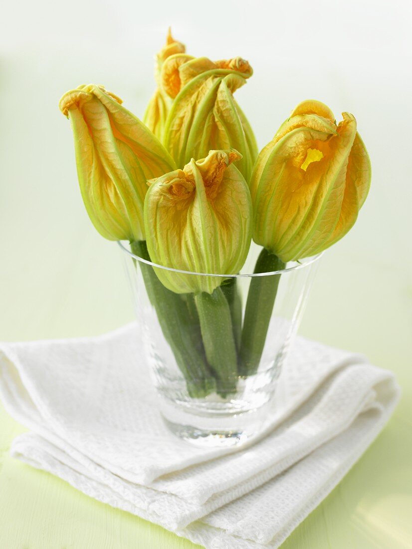 Fünf Zucchini mit Blüten in einem Glas auf Serviette