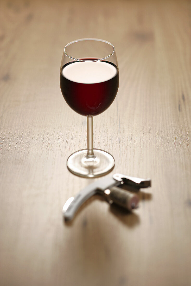 A glass of red wine with corkscrew and cork