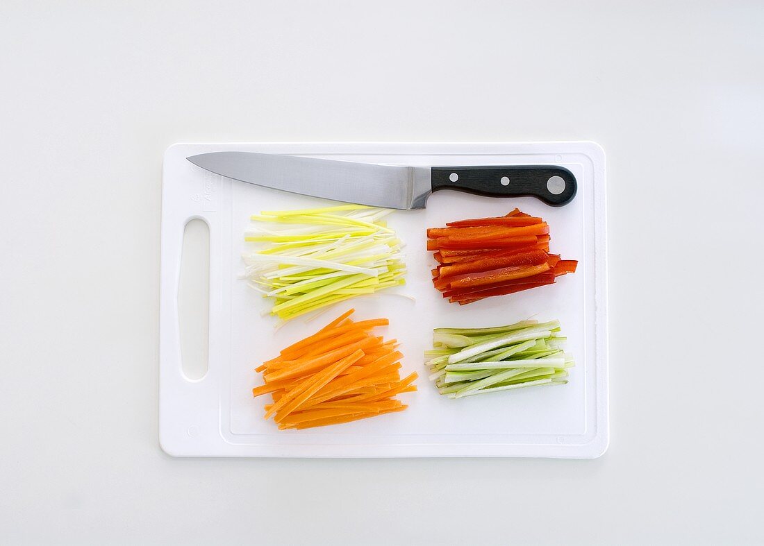 Julienne vegetables on a chopping board with a knife