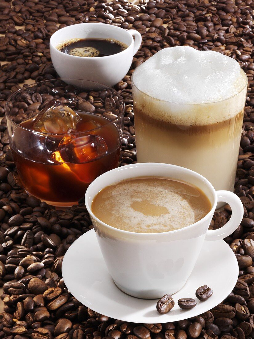 Vier verschiedene Kaffeegetränke auf Kaffeebohnen