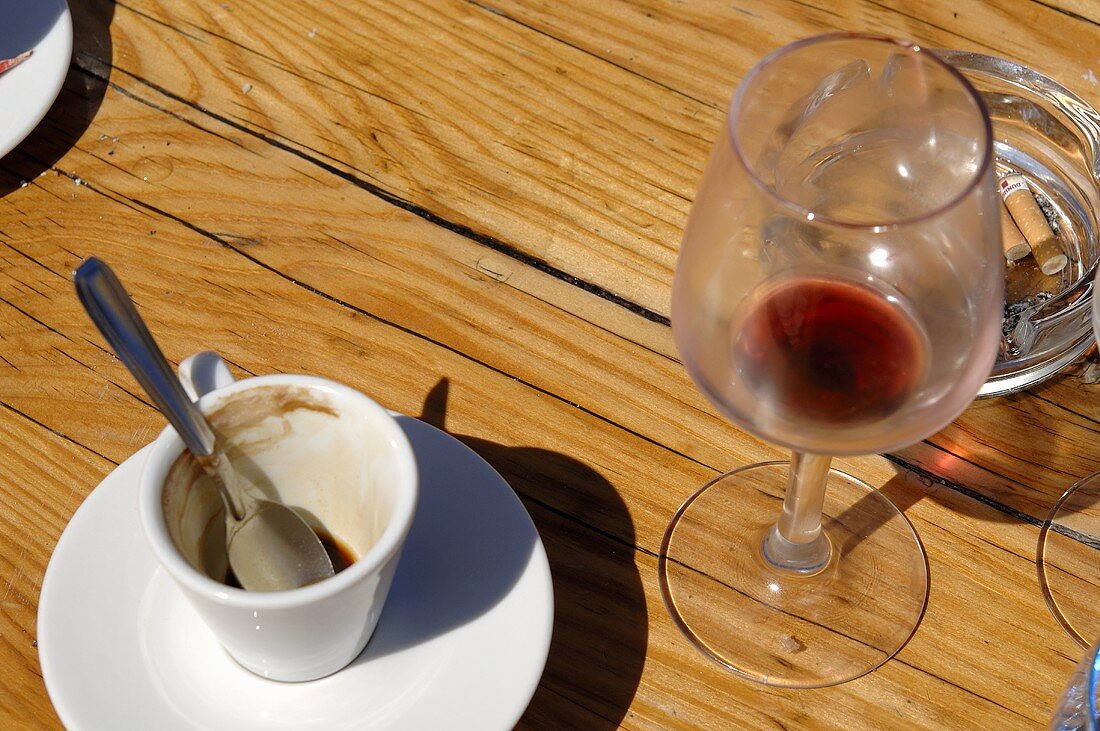 Leere Espressotasse, Rotweinglas und ein Aschenbecher