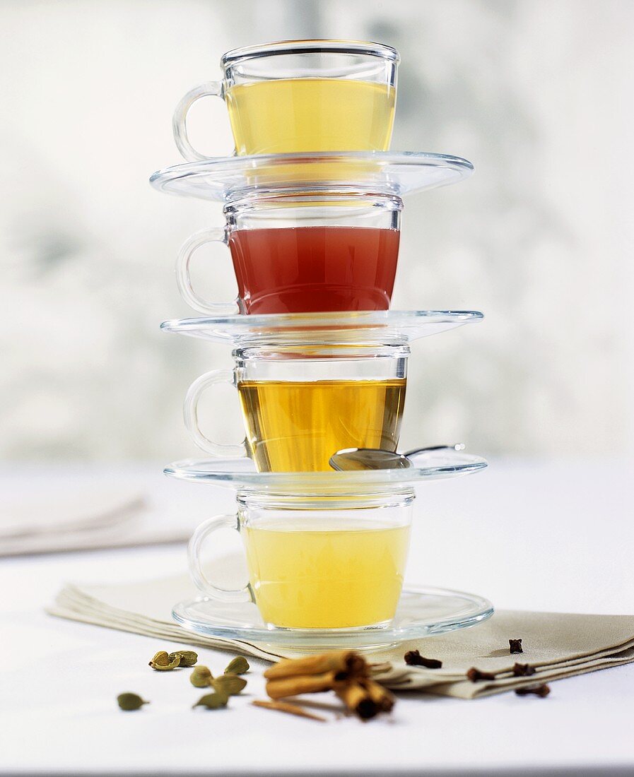 Four glass cups & saucers, each with a different tea, stacked