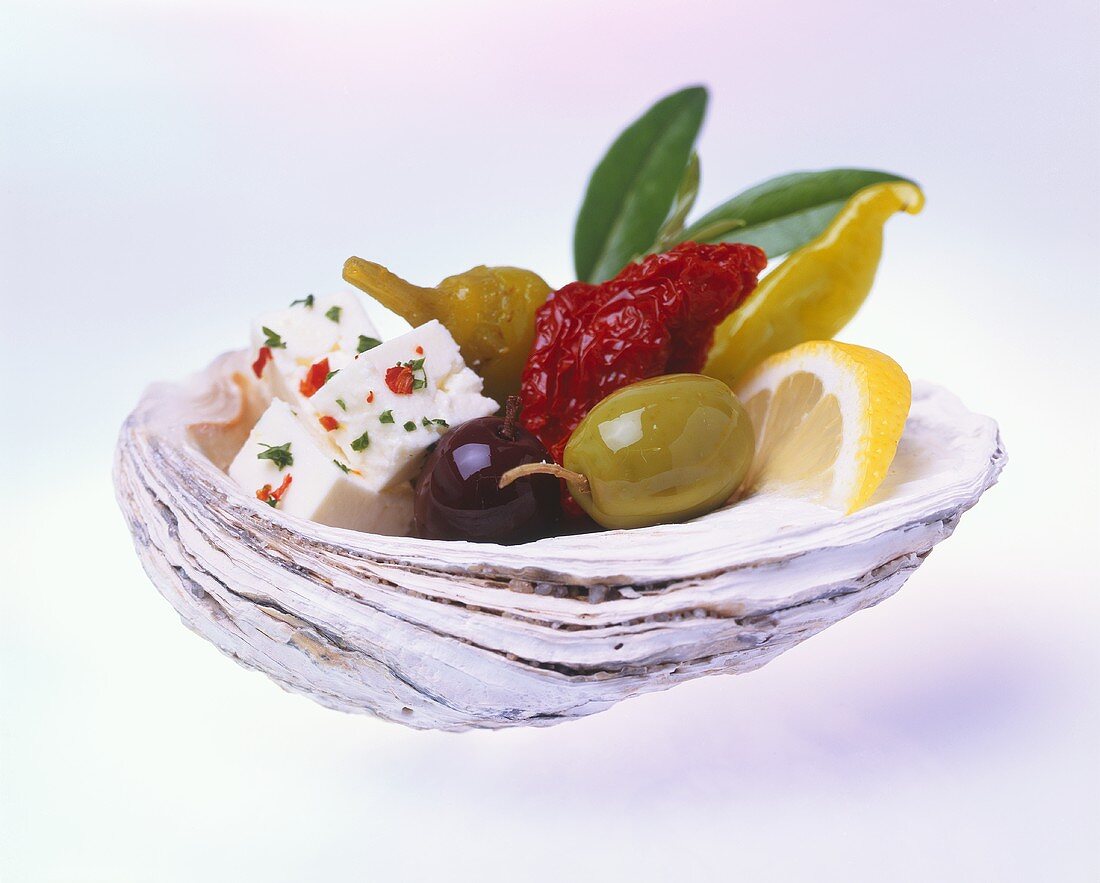 Feta mit Oliven und Peperoni in einer Muschelschale
