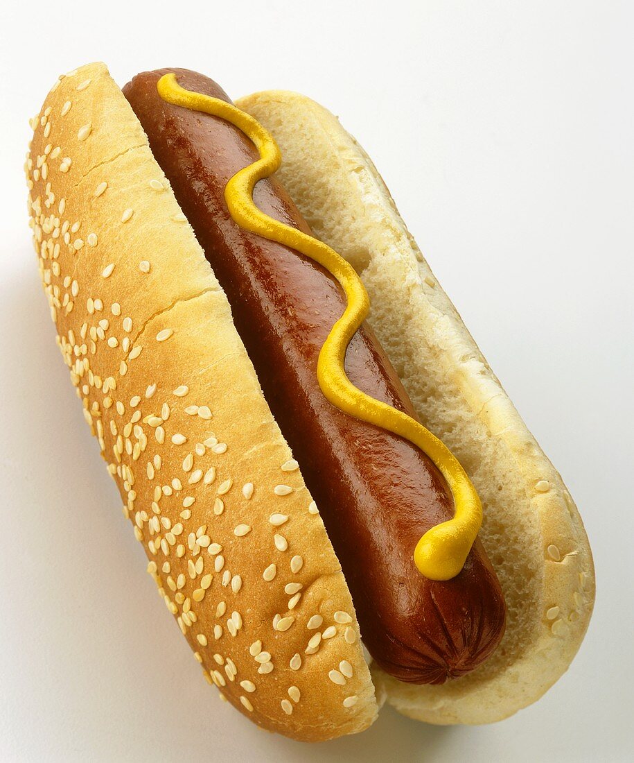 A hot dog with mustard in sesame bun