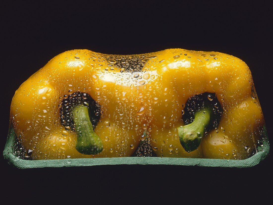 Zwei in Folie verpackte gelbe Paprikaschoten, Wassertropfen