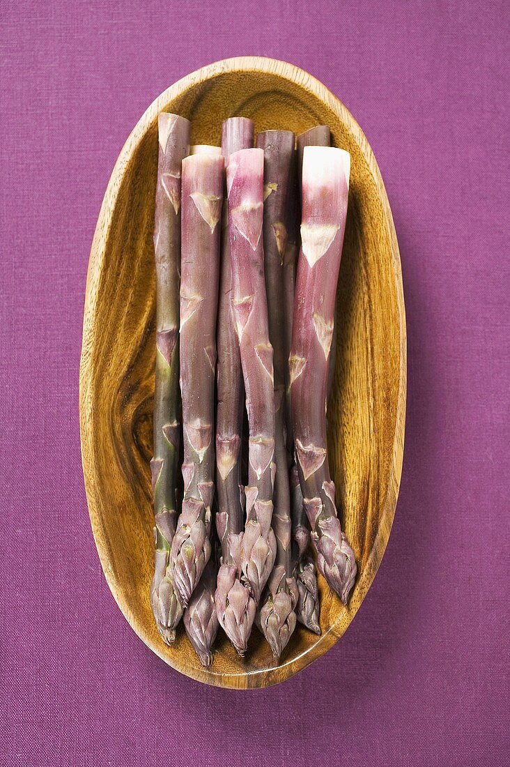 Purple asparagus in wooden bowl (overhead view)