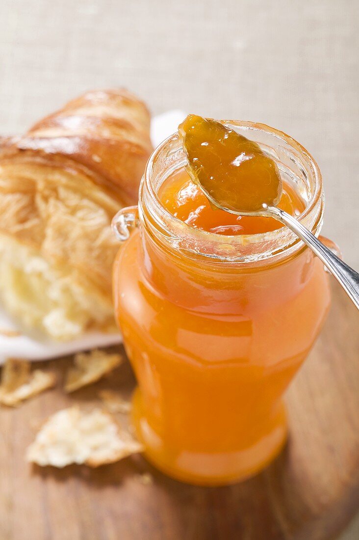 Aprikosenmarmelade im Glas mit Löffel, Croissant