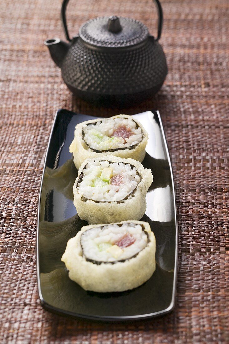 Maki sushi with tuna, cucumber and avocado in front of teapot