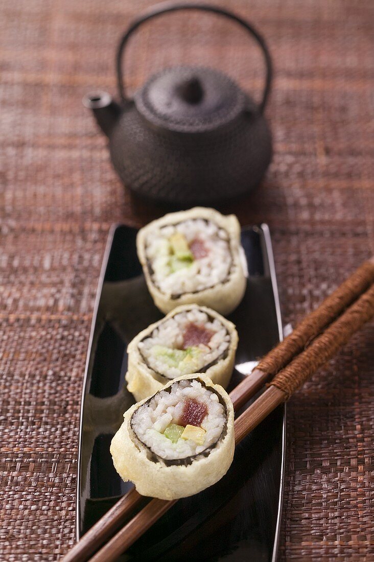 Maki-Sushi mit Thunfisch, Gurke und Avocado vor Teekanne