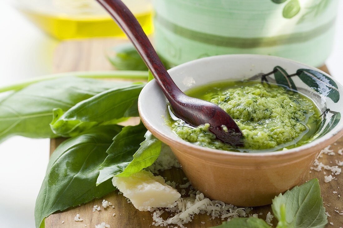 Pesto with olive oil in small bowl, basil, Parmesan