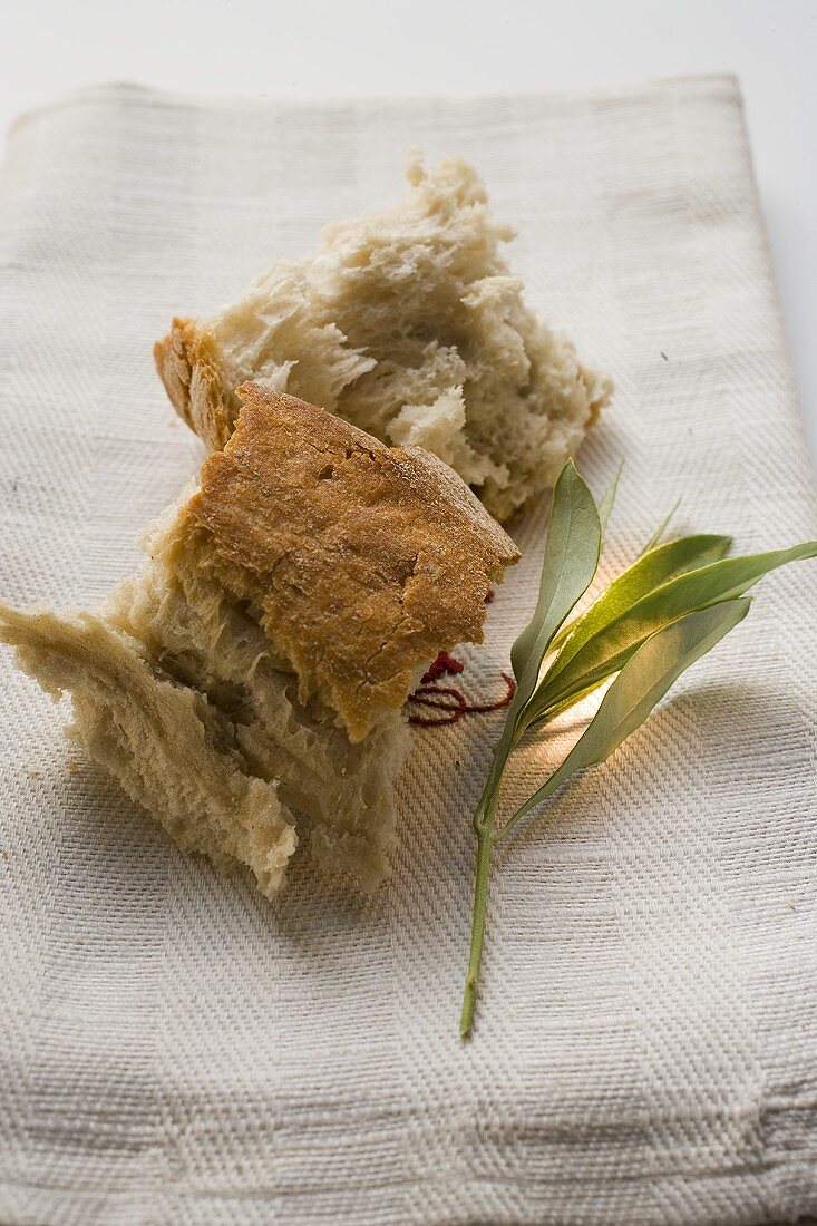 Weissbrotstücke auf Leinentuch neben Olivenzweig