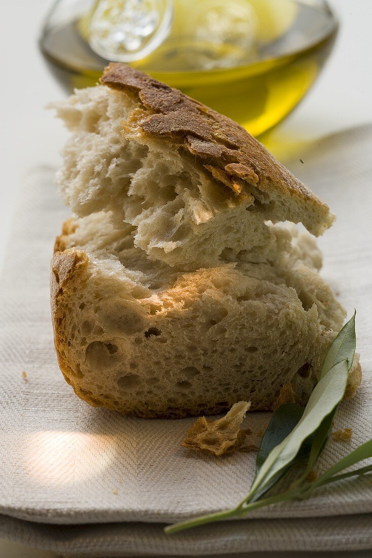 Weissbrotstücke auf Leinentuch mit Olivenzweig, Olivenöl