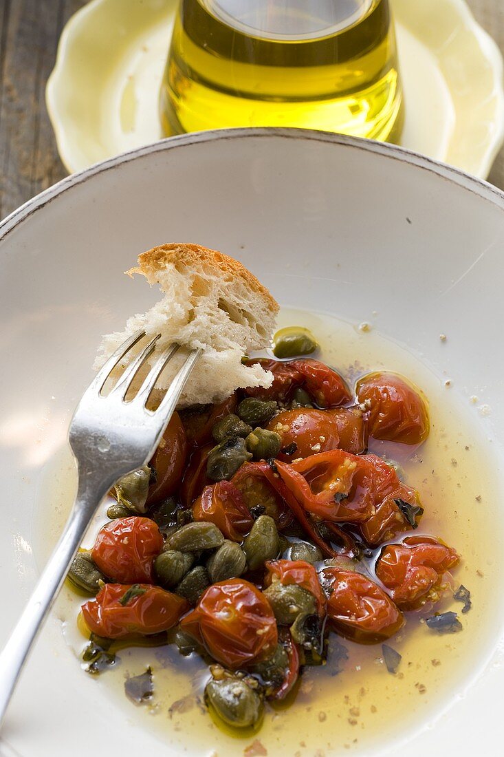 Roasted tomatoes with capers, white bread on fork, olive oil