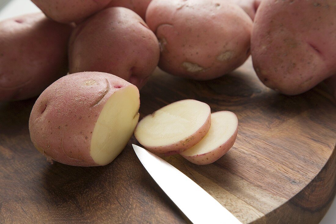 Red potatoes, one partly sliced, on wooden board