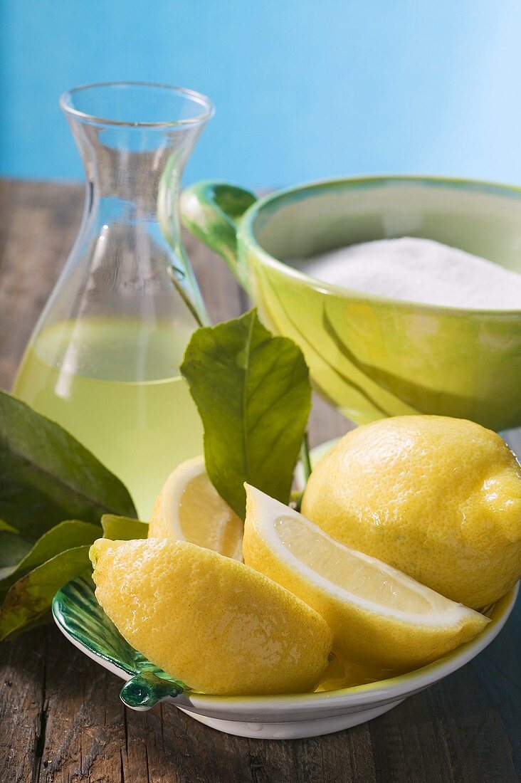 Frische Zitronen mit Blättern, Zitronensaft und Zucker