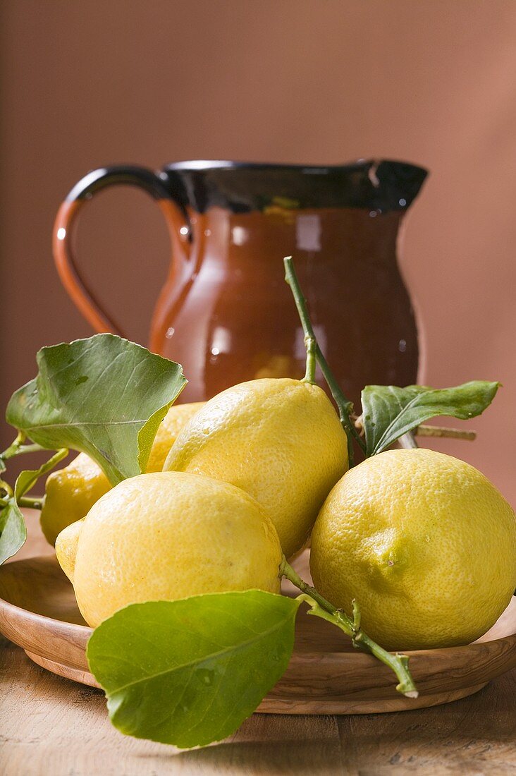 Frische Zitronen mit Blättern auf Teller vor Tonkrug