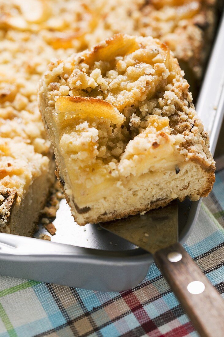 Apfel-Streusel-Kuchen in Backform mit Stück auf Kuchenheber