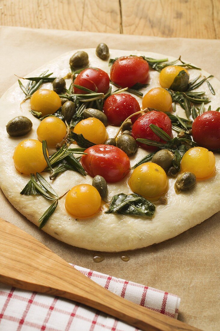 Unbaked pizza with cherry tomatoes, capers & rosemary