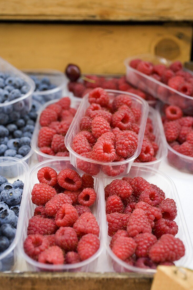 Raspberries and blueberries in plastic punnets at a market