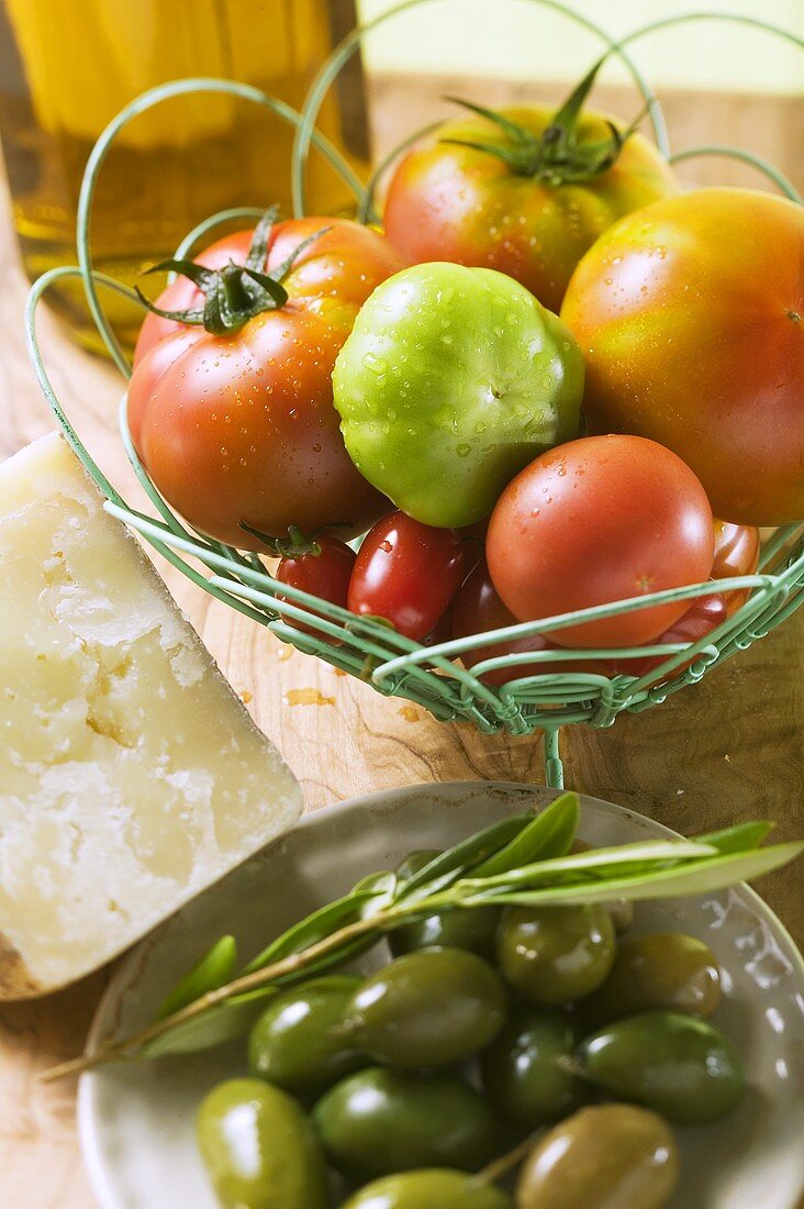 Verschiedene Tomaten im Drahtkorb, Oliven, Käse
